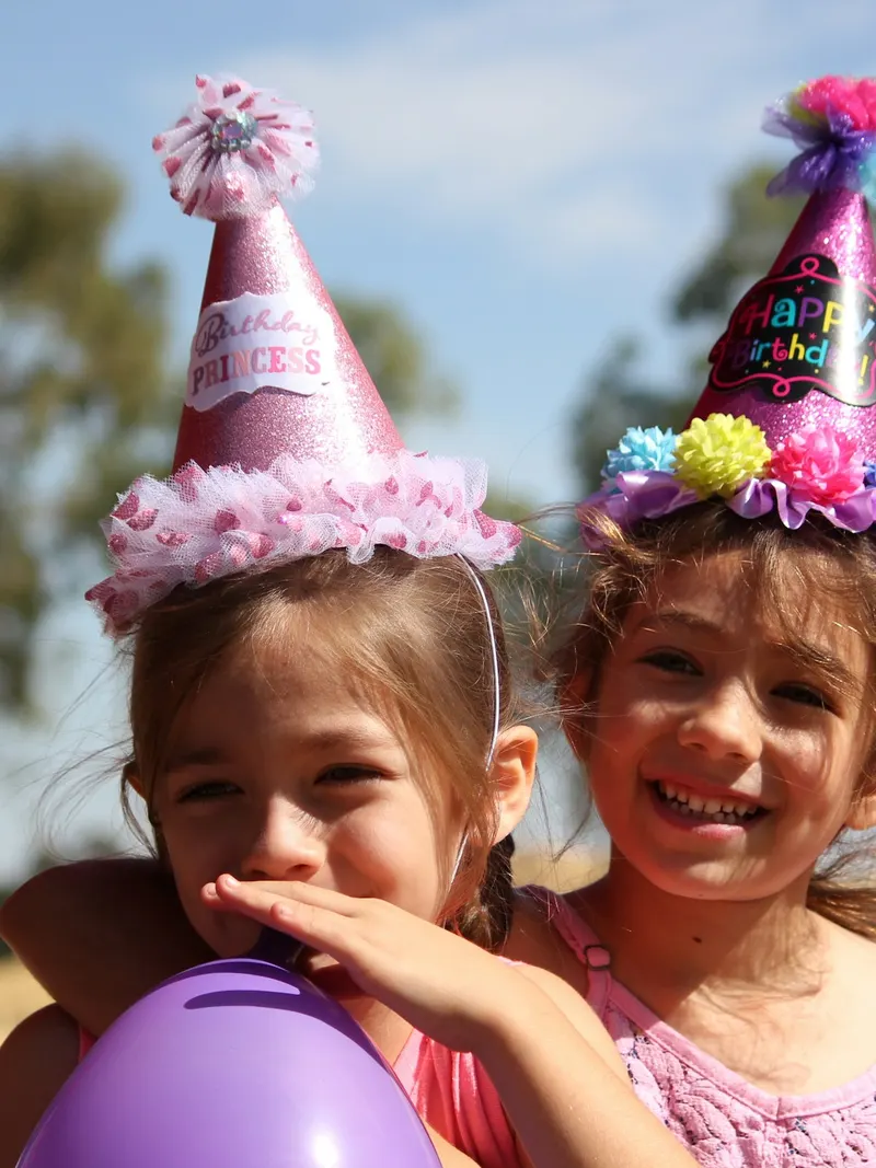 Zwei Mädchen mit Partyhüten und Luftballon lachen beim Kindergeburtstag