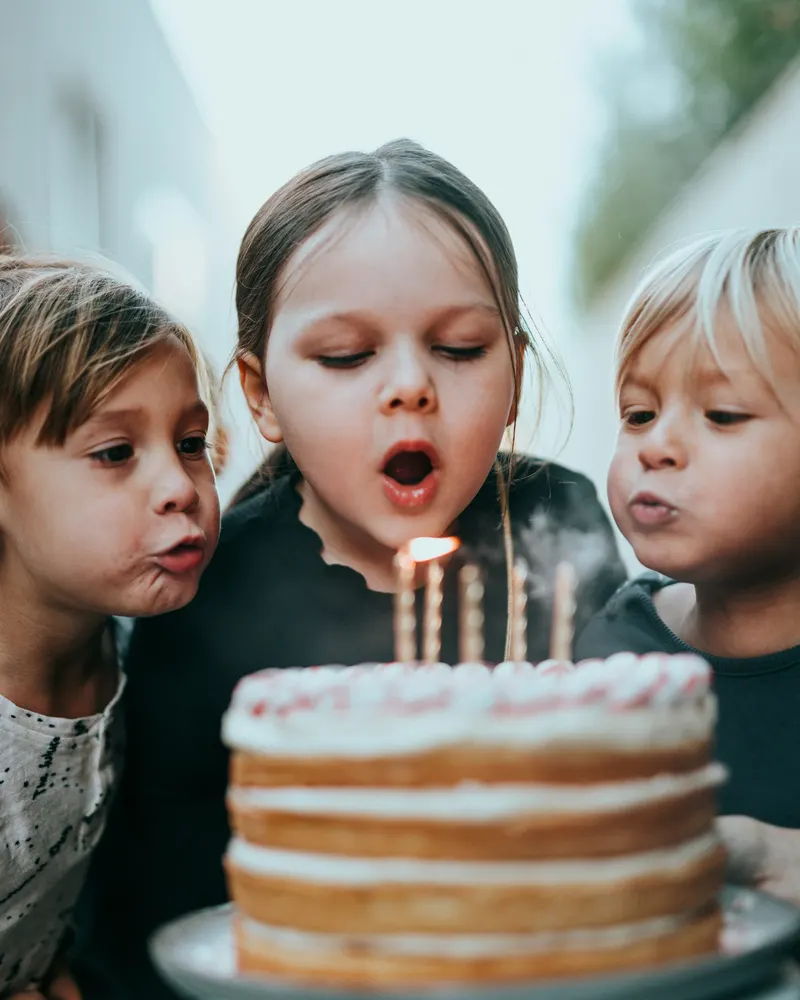 Kinder pusten gemeinsam die Kerzen auf der Geburtstagstorte aus