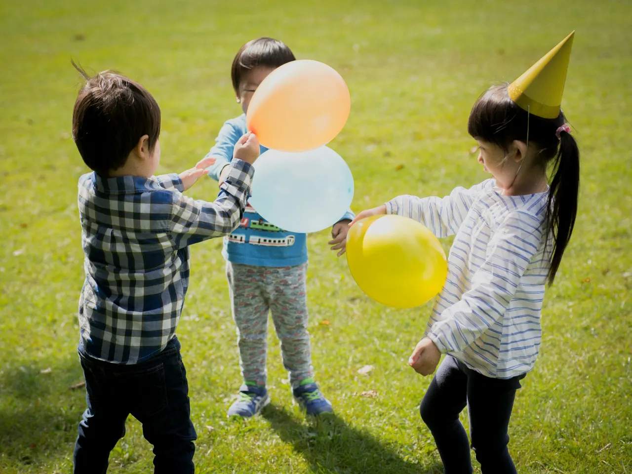 Kinder spielen mit Luftballons und Partyhut auf der Wiese