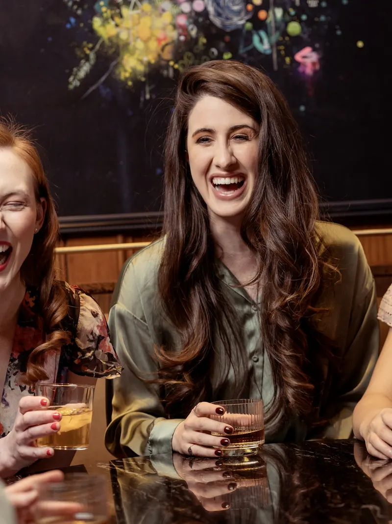 Freundinnen lachen gemeinsam mit Drinks am Tisch