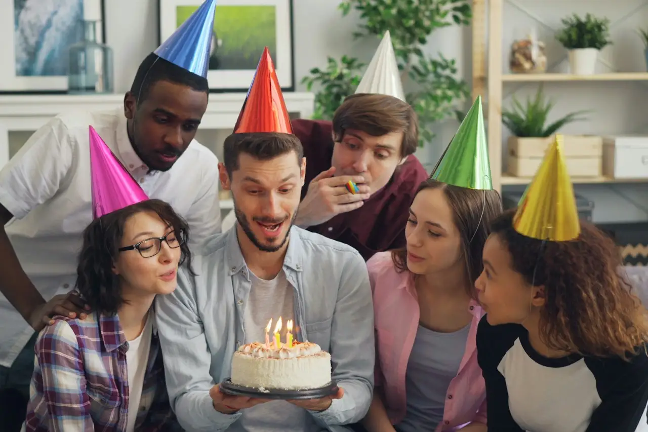 Freund:innen mit Partyhüten um eine Geburtstagstorte