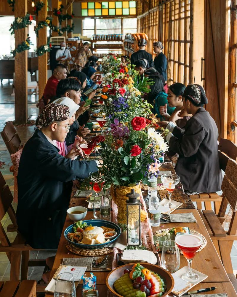 Gäste an einer langen Tafel mit Essen und Blumen